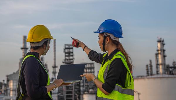 Two refinery workers in front of a plant
